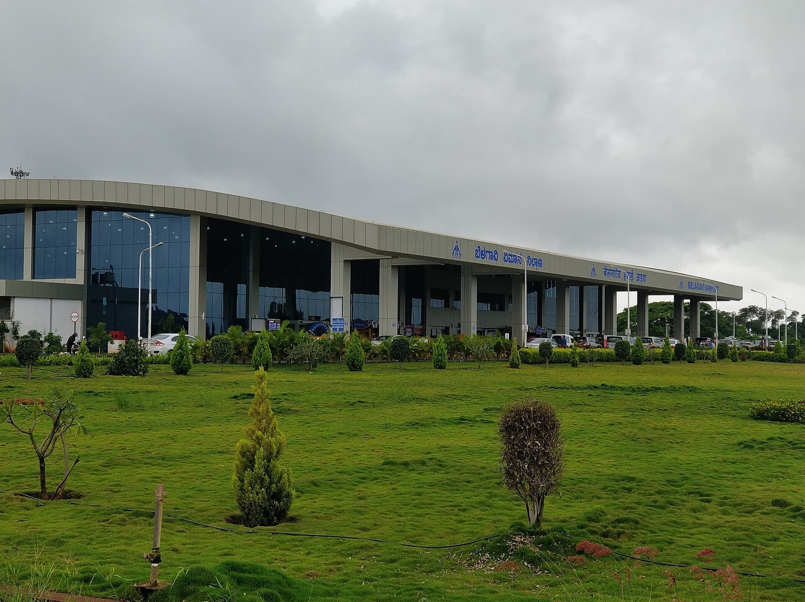 The terminal building of Belagavi Airport behind a lawn under a cloudy sky