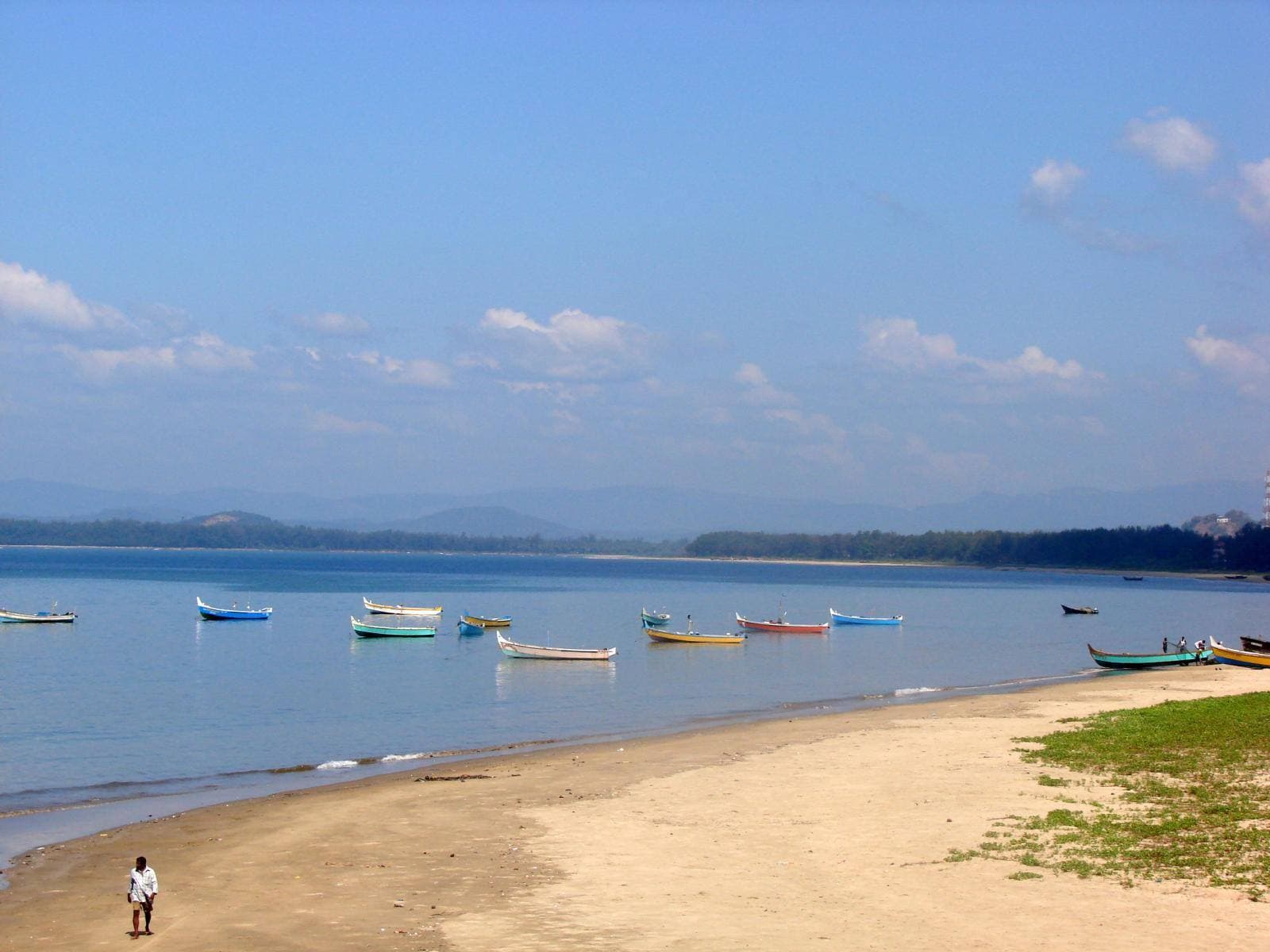 A sandy beach with boats on calm water at Karwar