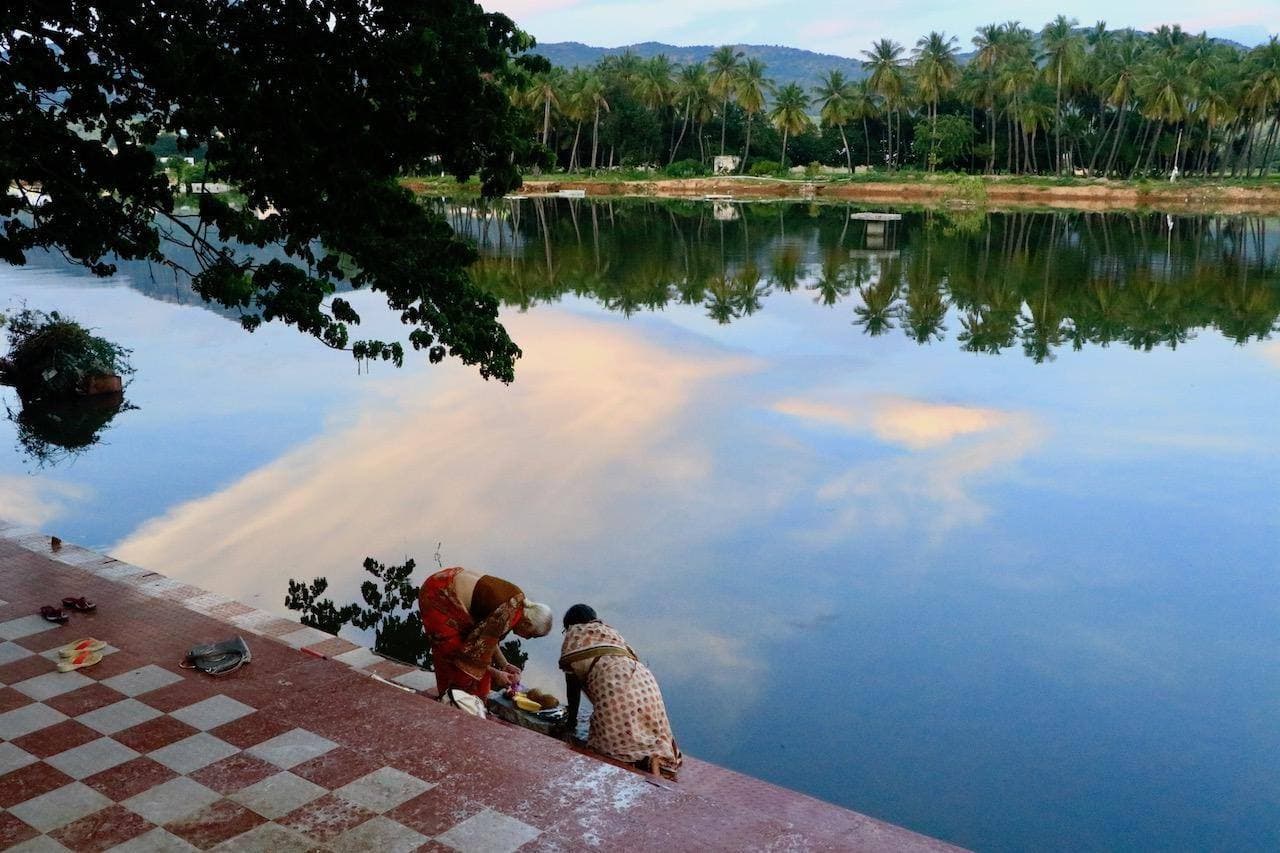 A lake reflecting palm trees and clouds at Puttaparthi