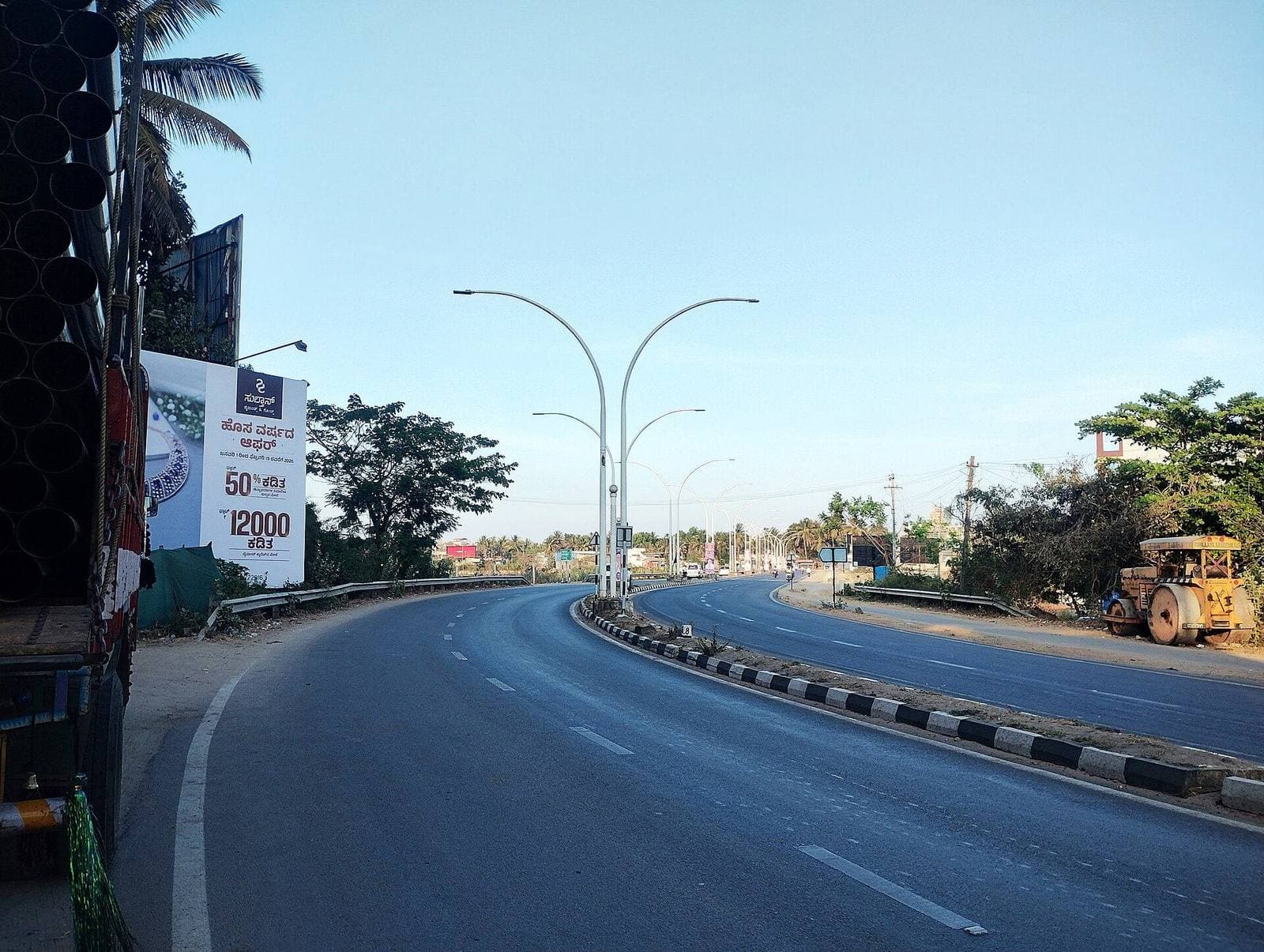 A wide road curving past trees in Shivamogga
