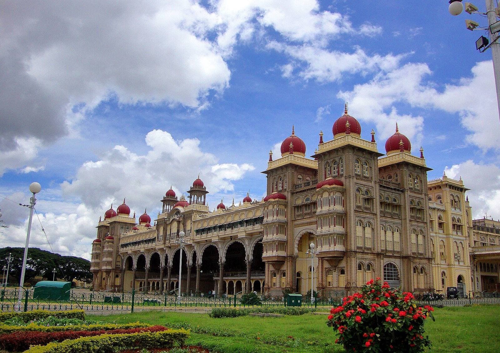 Mysore Palace with its red domes under a cloudy blue sky